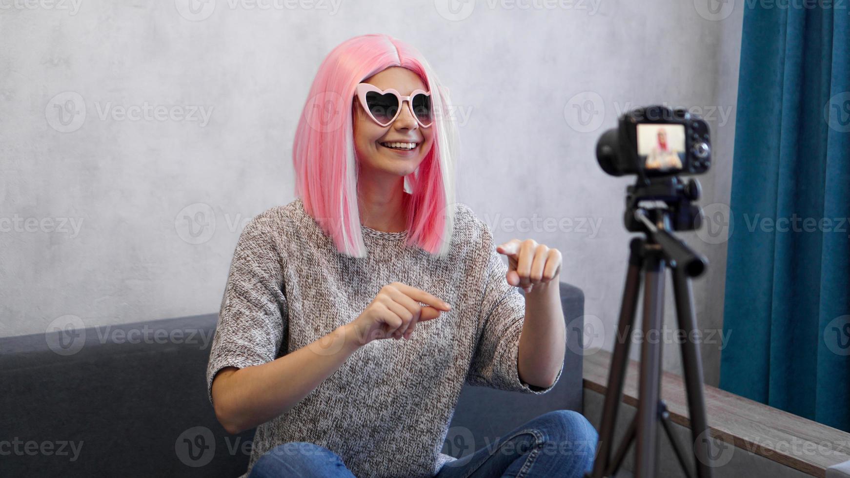 Happy girl blogger in pink wig in front of the camera on a tripod photo