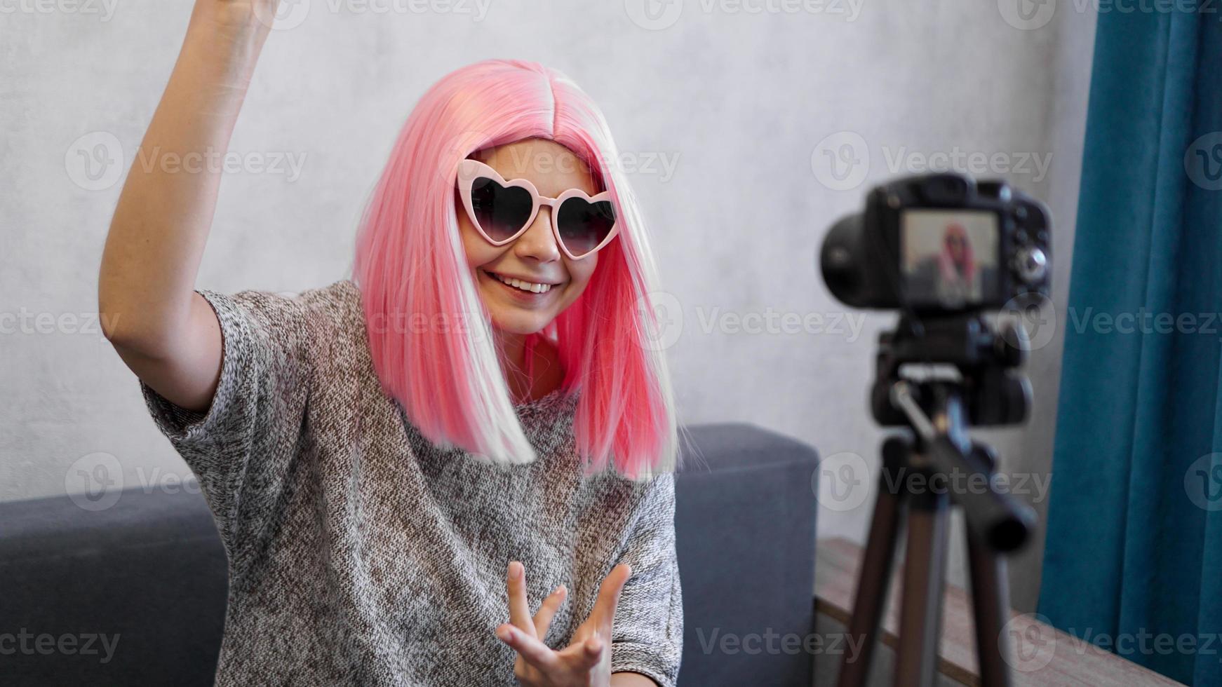 Blogger niña feliz en pelucas rosas delante de la cámara en un trípode foto