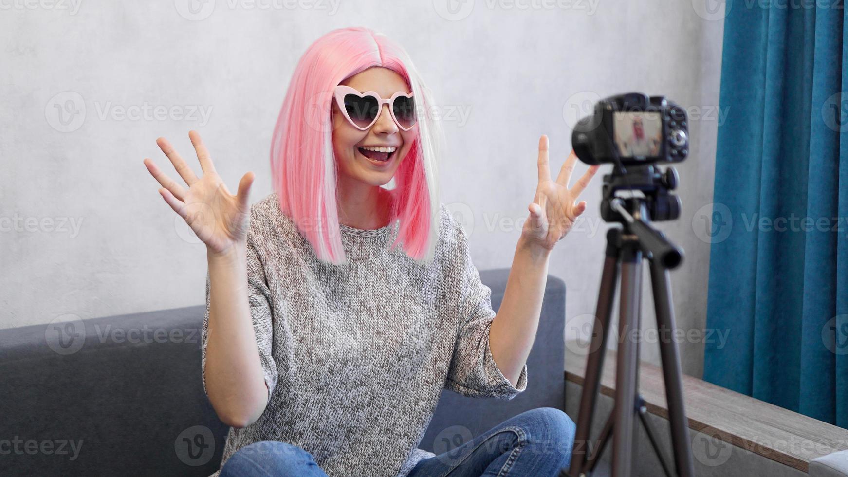 Happy girl blogger in pink wig in front of the camera on a tripod photo