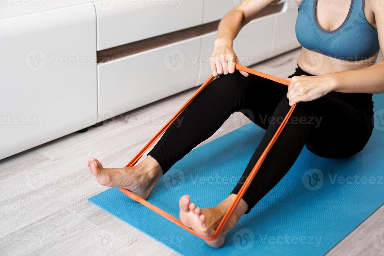 Young woman with elastic band. She trains her legs at home photo