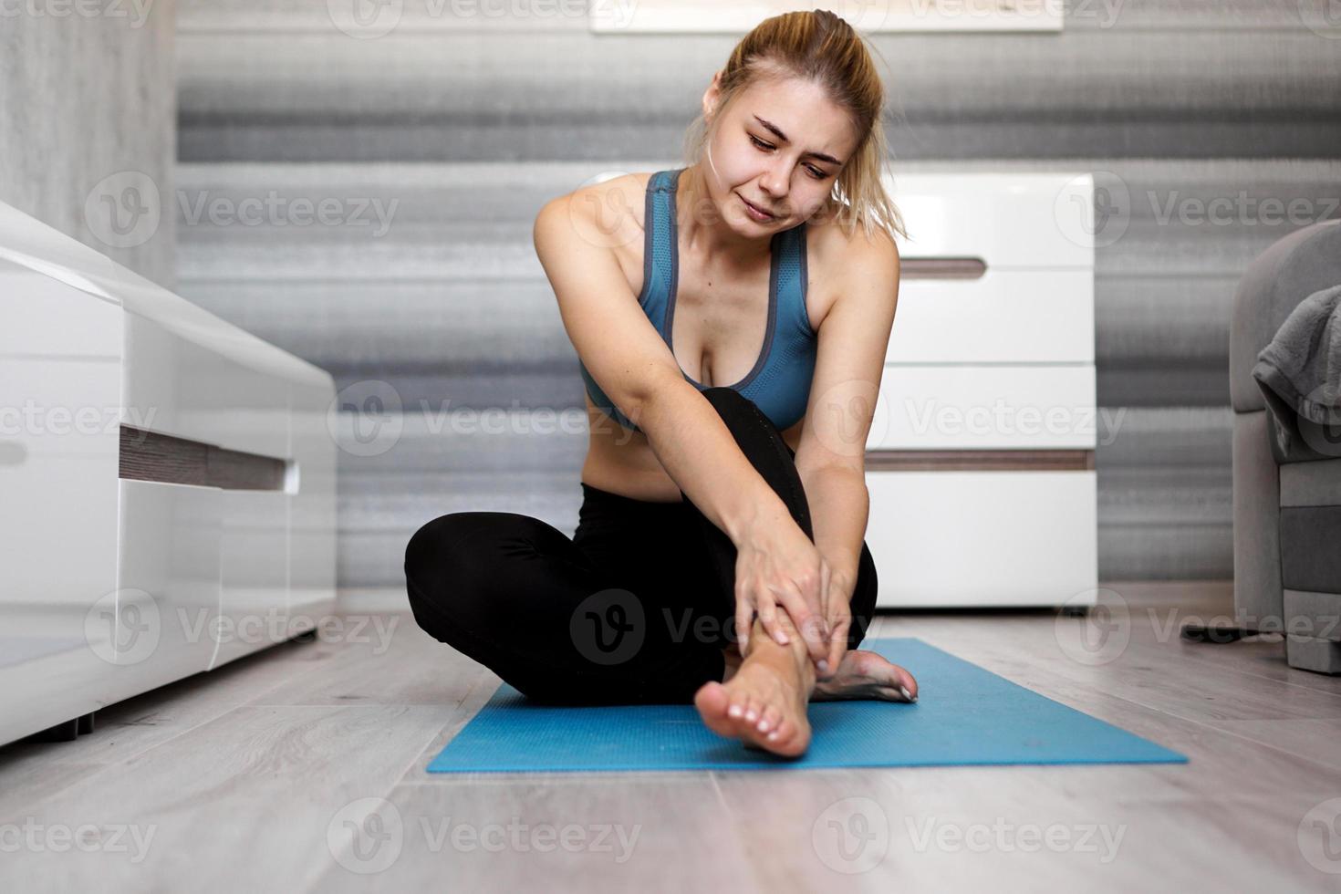 Infeliz mujer sentada en la estera de yoga con lesión en el tobillo, sintiendo dolor foto