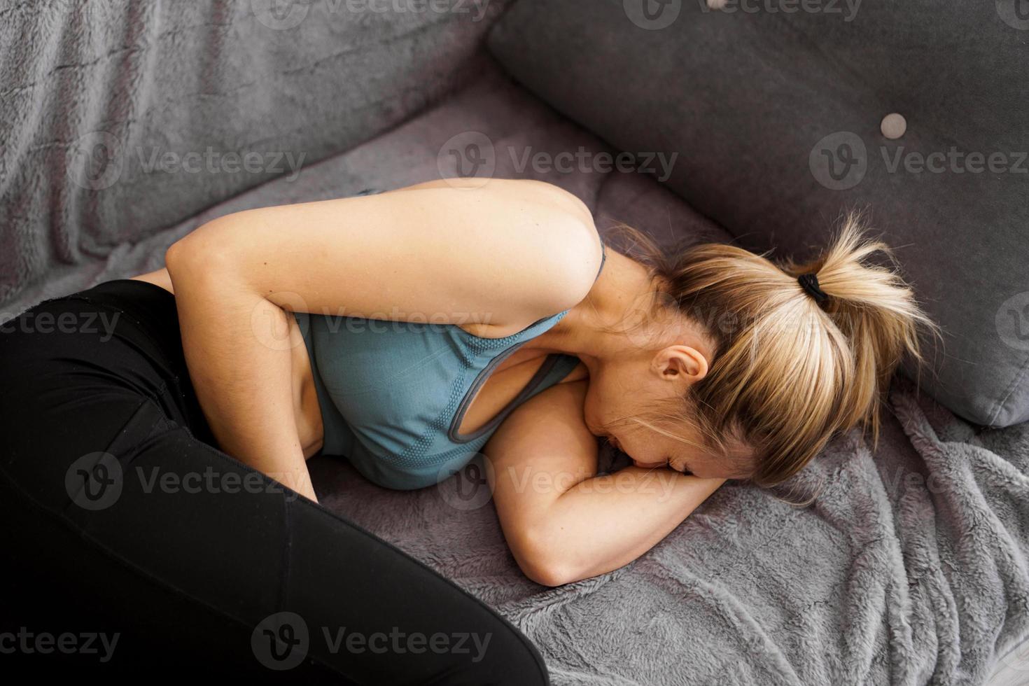 Vista lateral de la mujer que sufre de dolor de estómago acostado en el sofá en casa foto