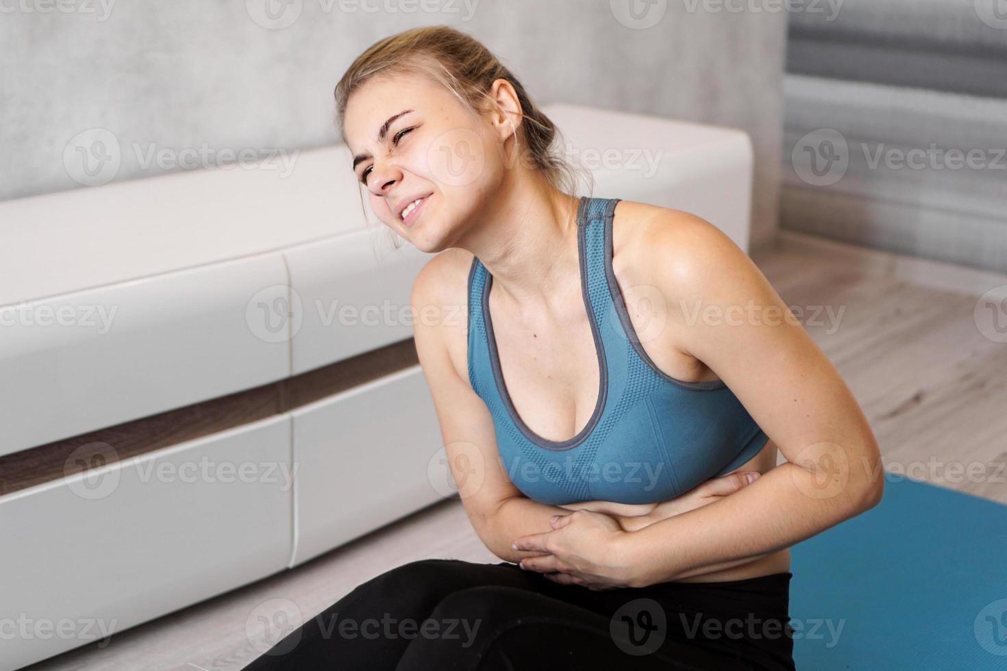 Portrait of young woman sitting on yoga mat, touching her stomach photo