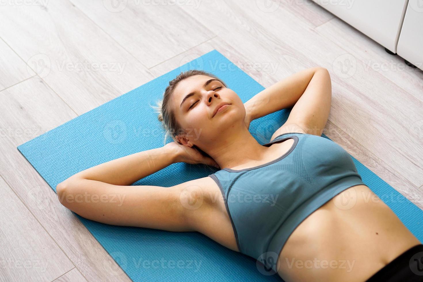 Top view of beautiful young woman lying on yoga mat after workout photo