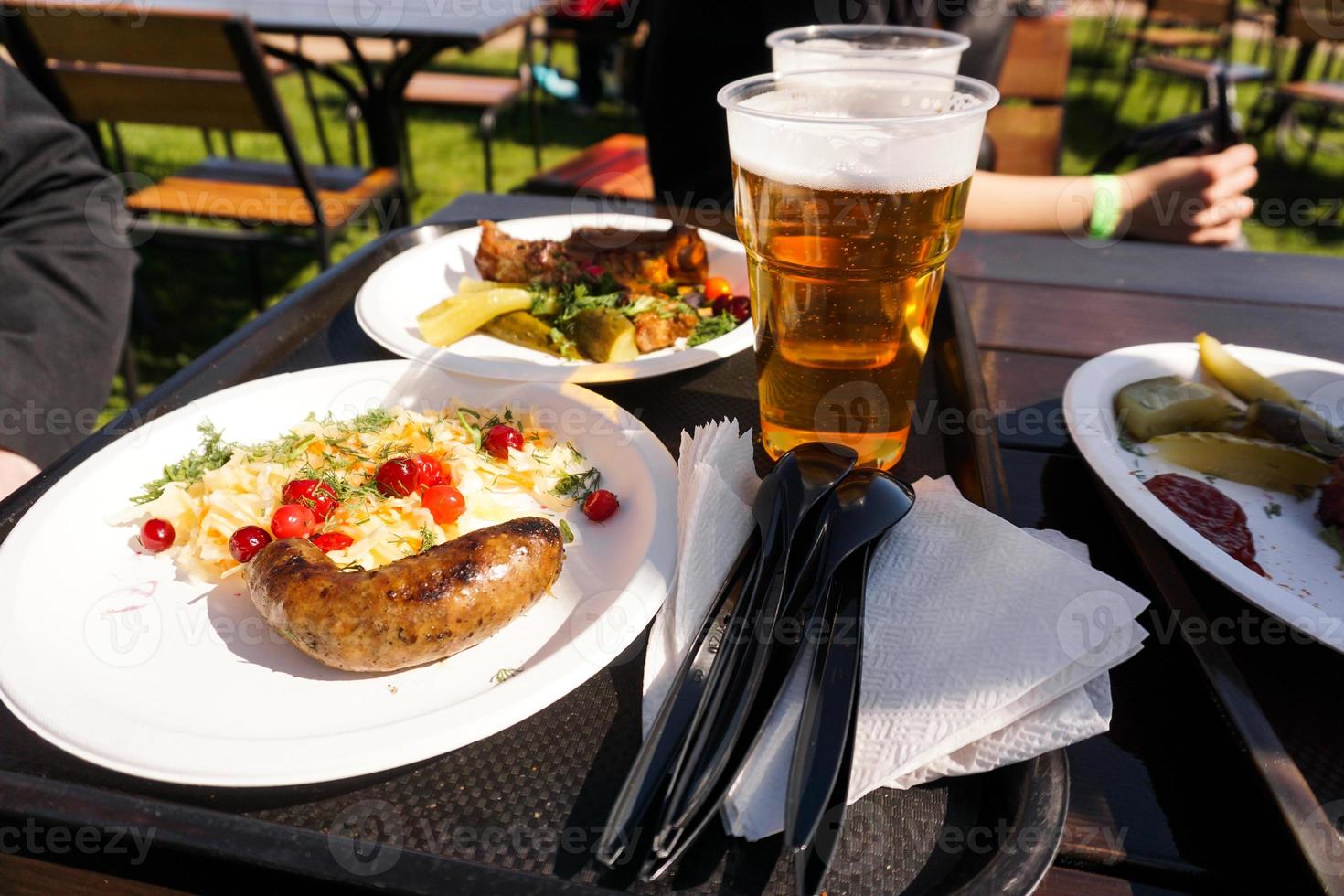 Sausage with salad on a plate and light beer on a tray. Street food photo