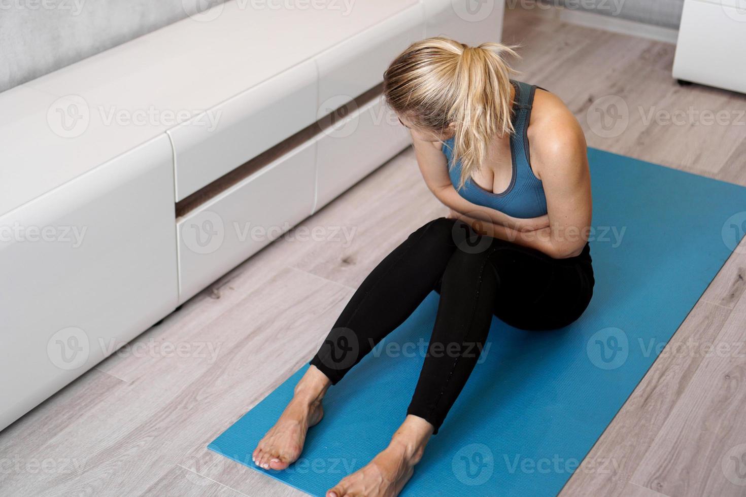 Fitness woman having pain in stomach during home workout photo