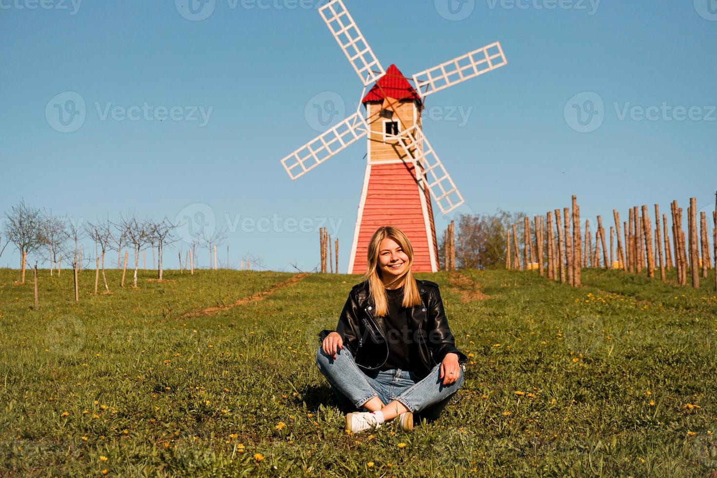 Hermosa joven sentada en la hierba contra el molino foto