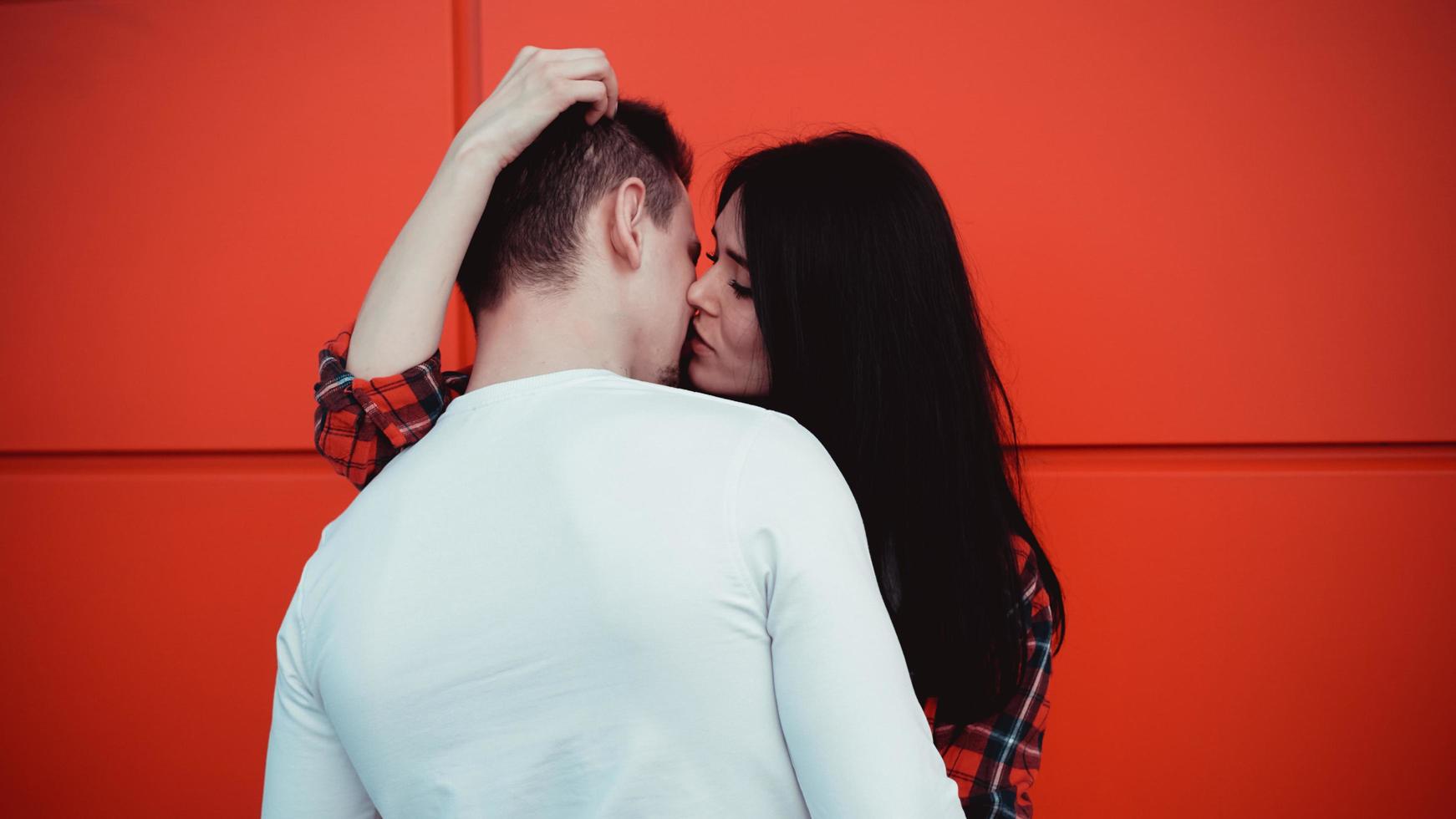 Pareja besándose contra la pared roja aislada en la ciudad foto