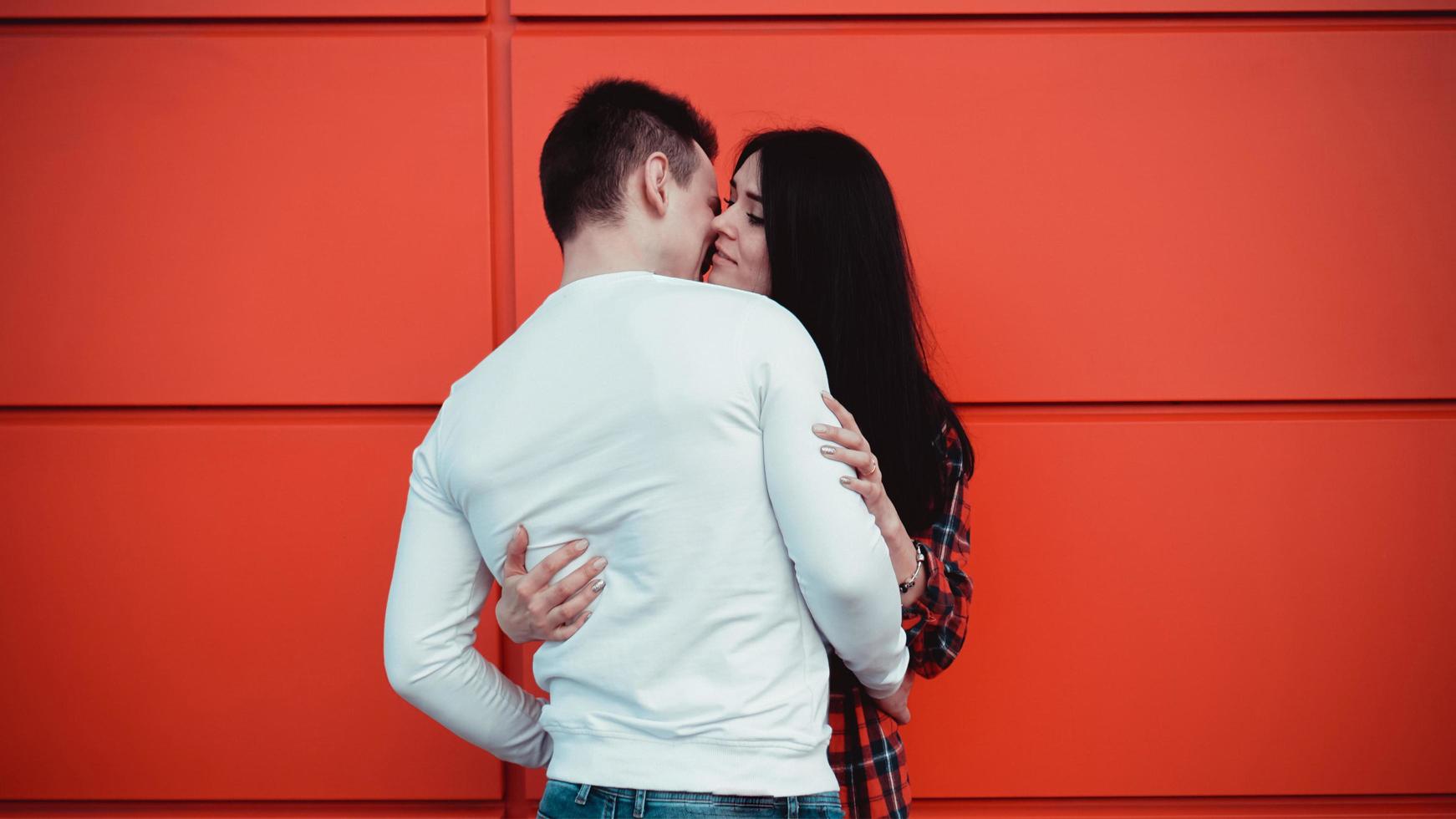 Pareja besándose contra la pared roja aislada en la ciudad foto