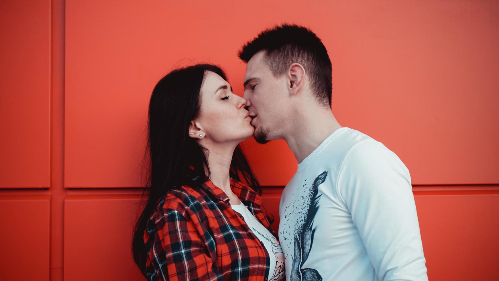 Pareja besándose contra la pared roja aislada en la ciudad foto