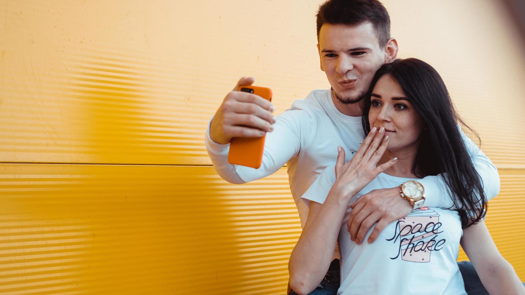 Encantadora pareja joven haciendo selfie en smartphone sobre fondo amarillo foto