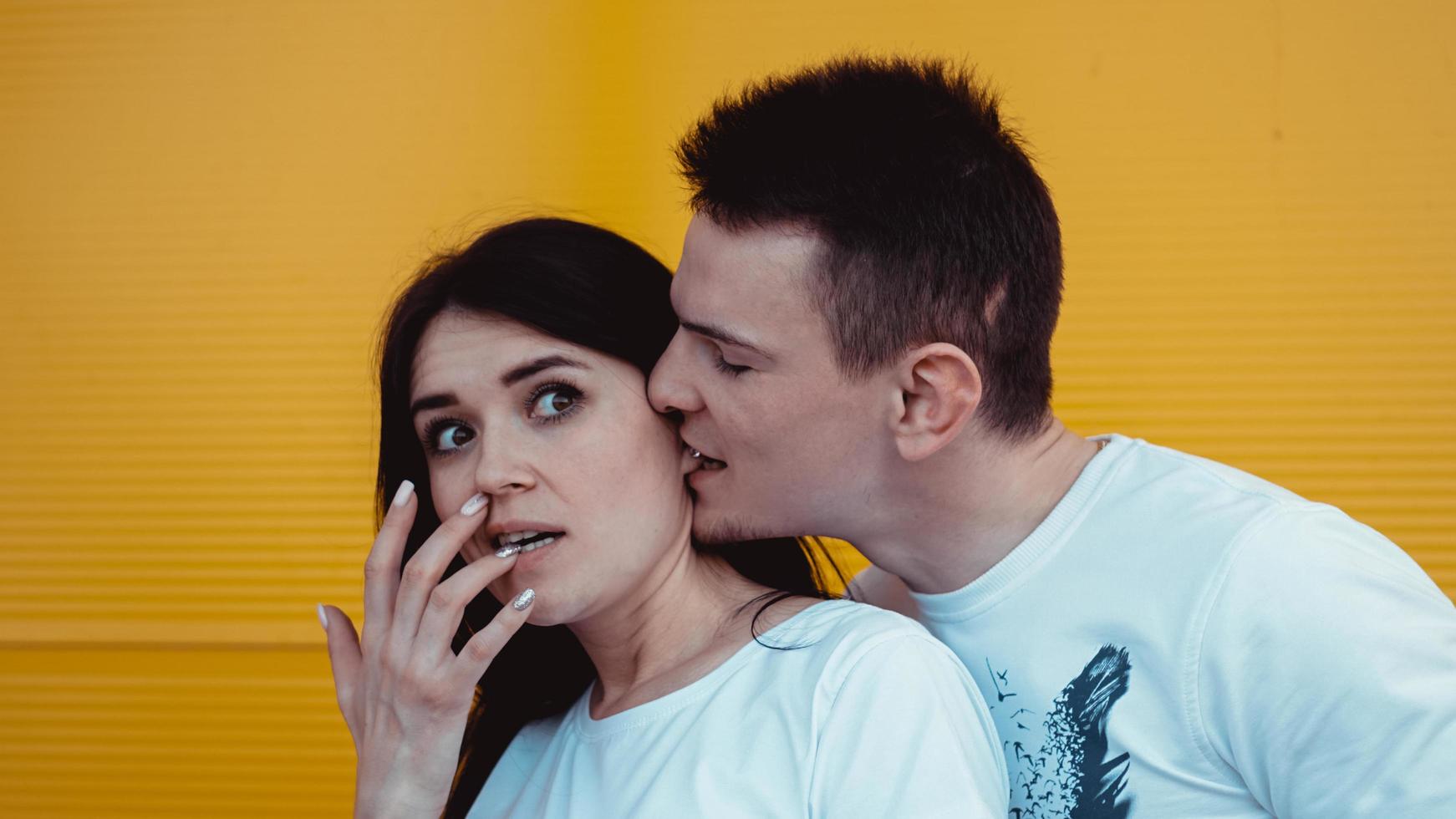 Funny young man bites his girlfriends ear and embracing her photo