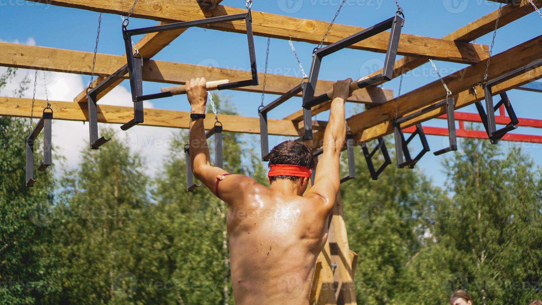 El hombre atravesando obstáculos durante la carrera de obstáculos en el campo de entrenamiento foto