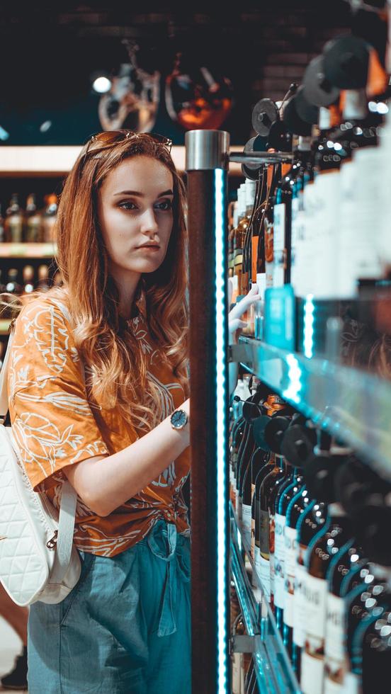 mujer joven está eligiendo vino en el supermercado. foto