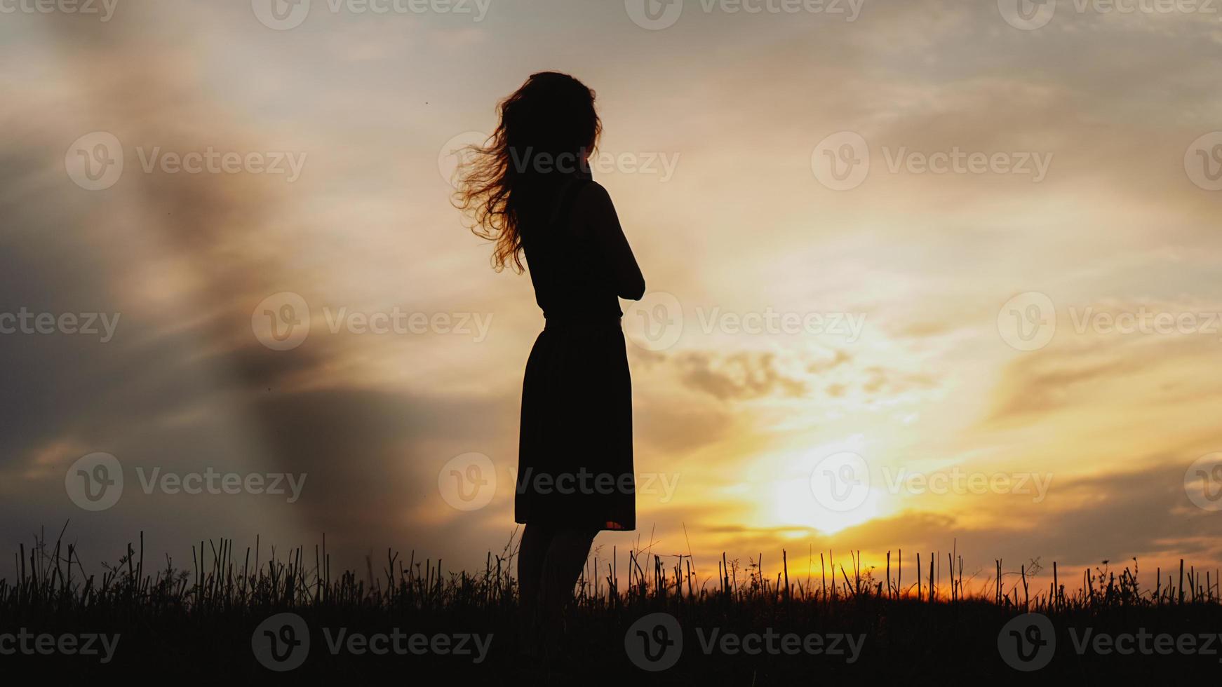 silueta, de, un, mujer joven, posición, en, pasto seco, campo, en, ocaso foto