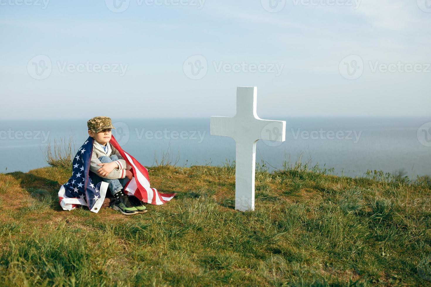 Un niño con una gorra militar, cubierto por la bandera de EE. UU. foto