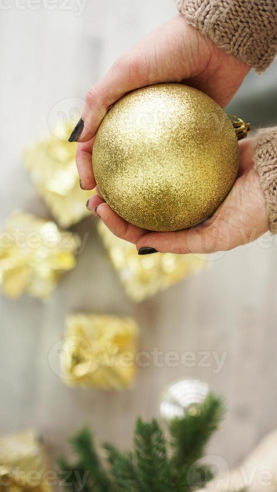 Mano sujetando adornos de bolas de oro sobre fondo de árbol de Navidad foto