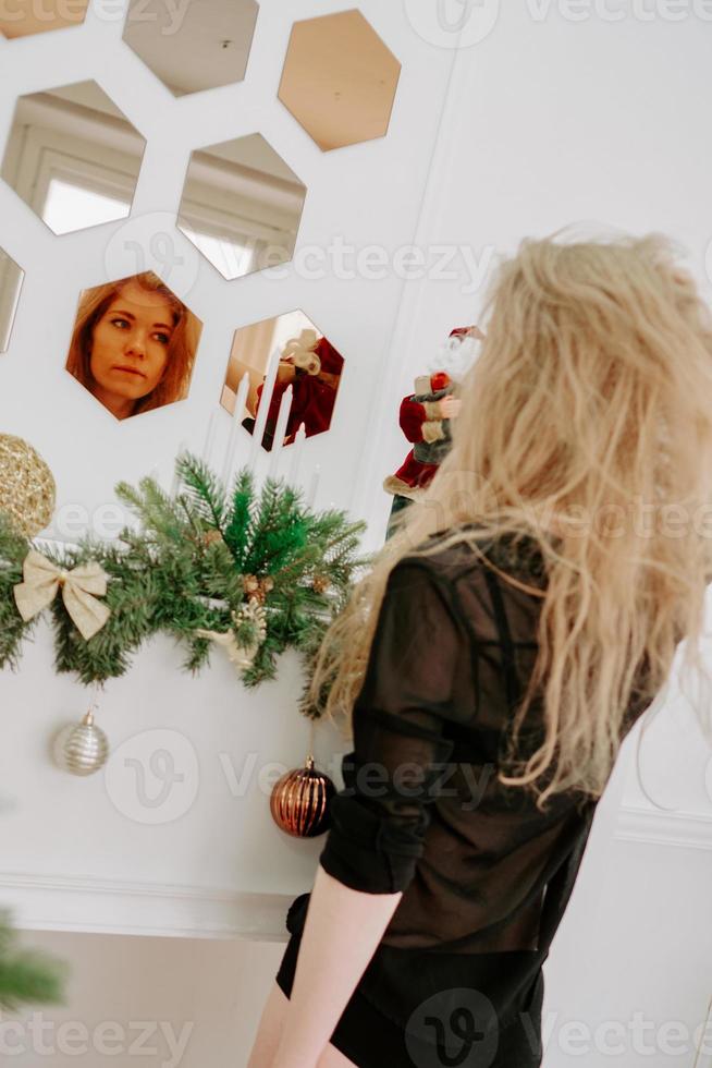 Una mujer bonita de cabello rubio en Navidad se encuentra cerca del espejo foto