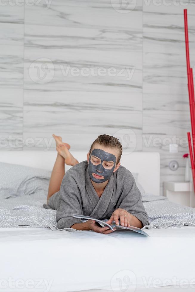 Mujer con mascarilla relajante acostado en la cama leyendo una revista foto