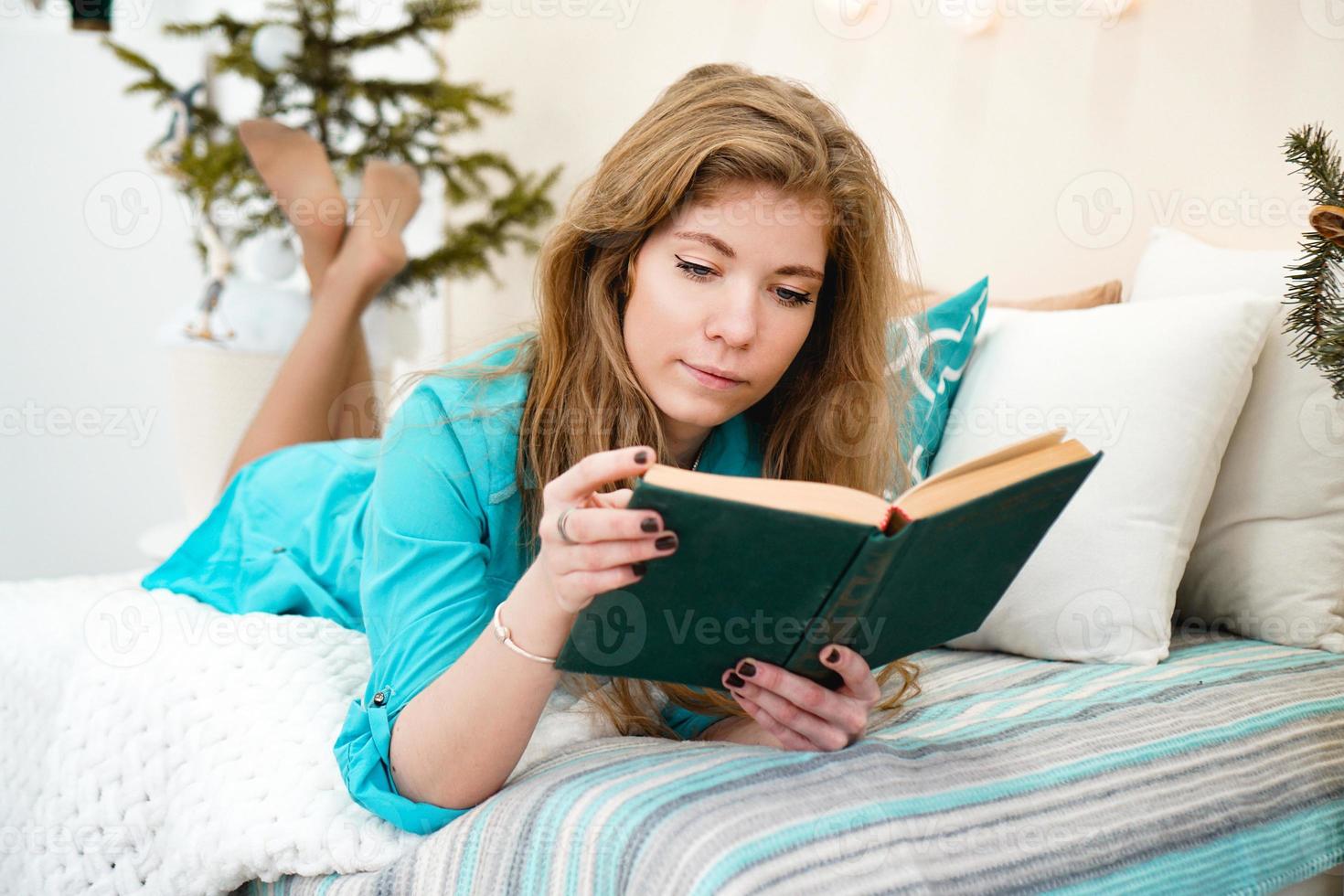 Young girl reading book while laying on bed at home photo