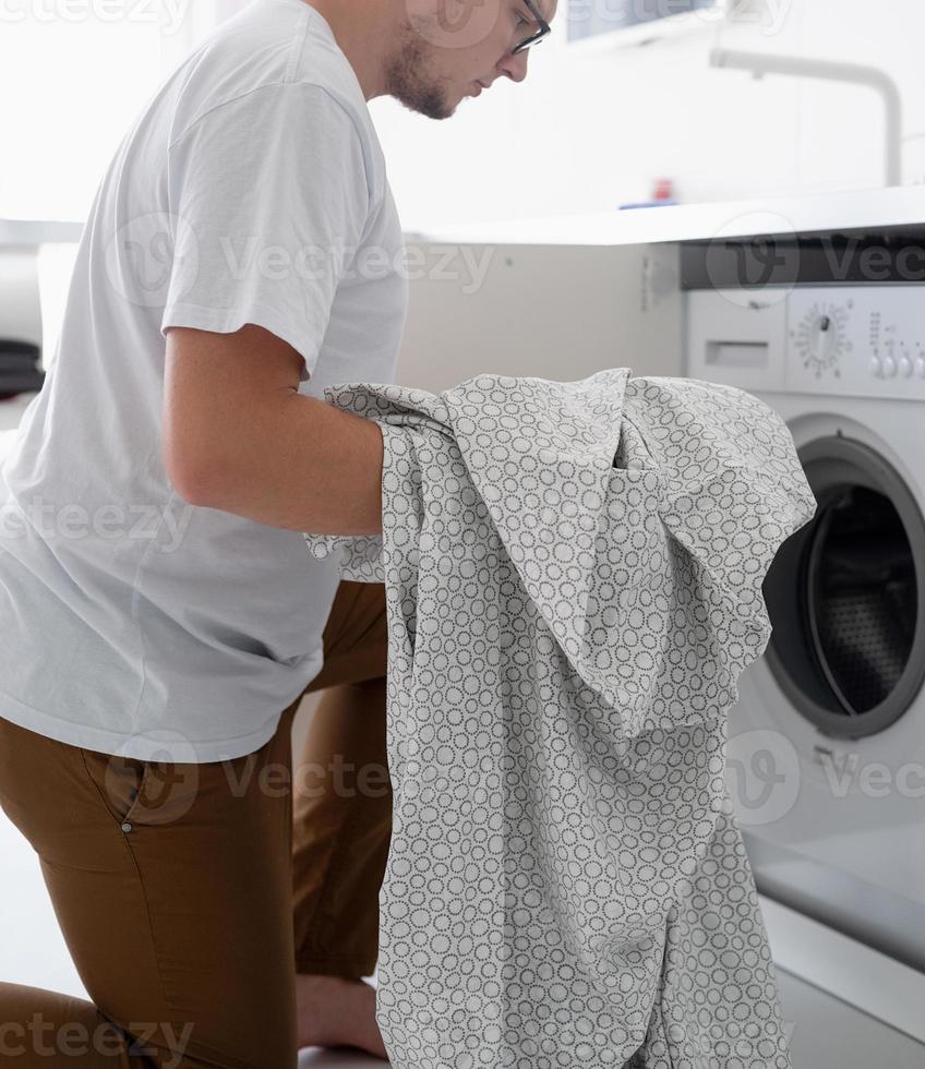 Young man putting clothes into washing machine photo