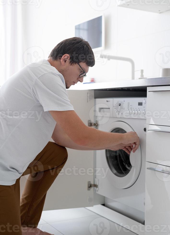 Young man putting clothes into washing machine photo