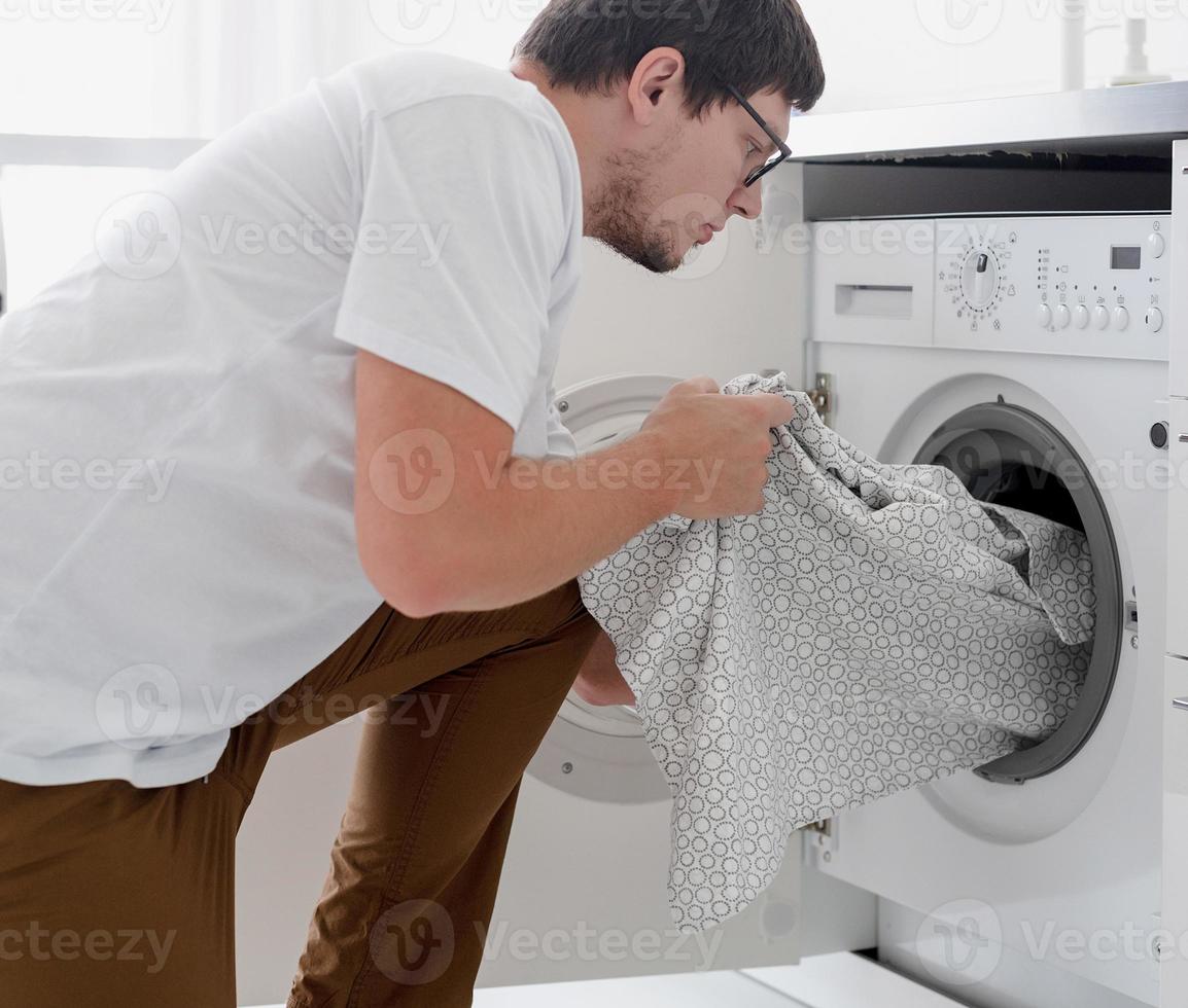 Young man putting clothes into washing machine photo