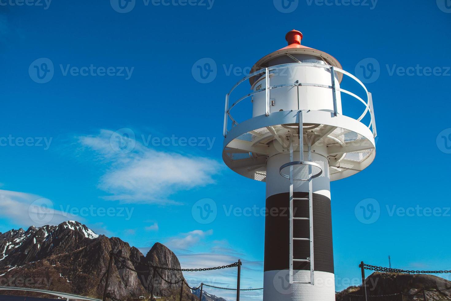 Lighthouse on the pier on the background of mountains and blue sky photo