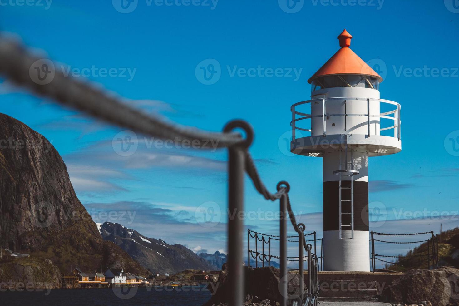 Lighthouse on the pier on the background of mountains and blue sky photo