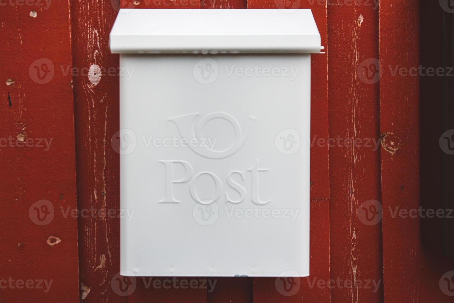 A white mailbox on a red wooden wall with a red door photo