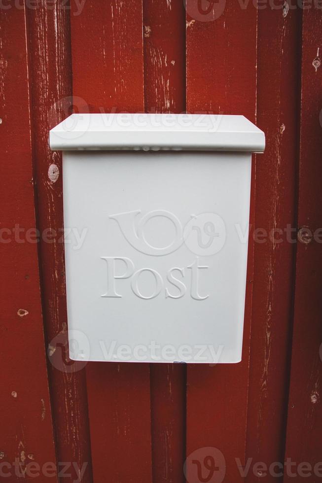 Un buzón blanco en una pared de madera roja con una puerta roja. foto