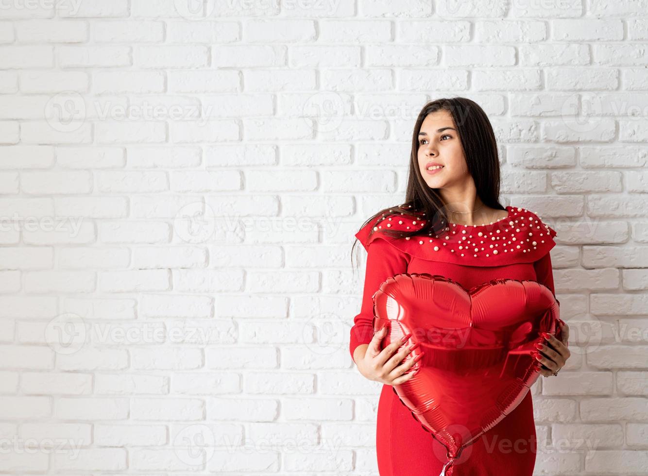 Joven mujer morena en vestido rojo sosteniendo un globo de corazón rojo foto
