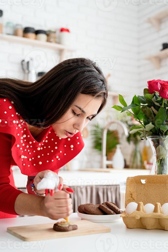 Mujer en vestido rojo haciendo galletas de San Valentín en la cocina foto