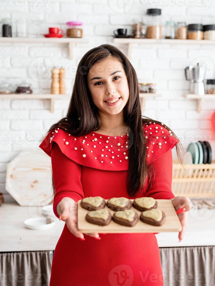 Mujer en vestido rojo haciendo galletas de San Valentín en la cocina foto