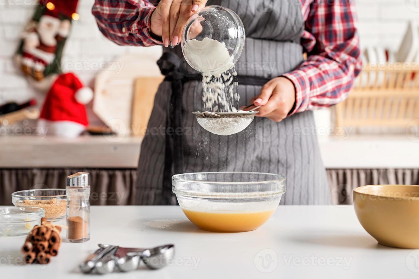 Joven latina vertiendo harina en la masa cocinar en la cocina foto