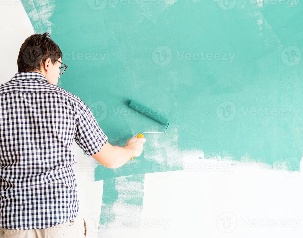 Hombre coloreando la pared verde con un rodillo foto