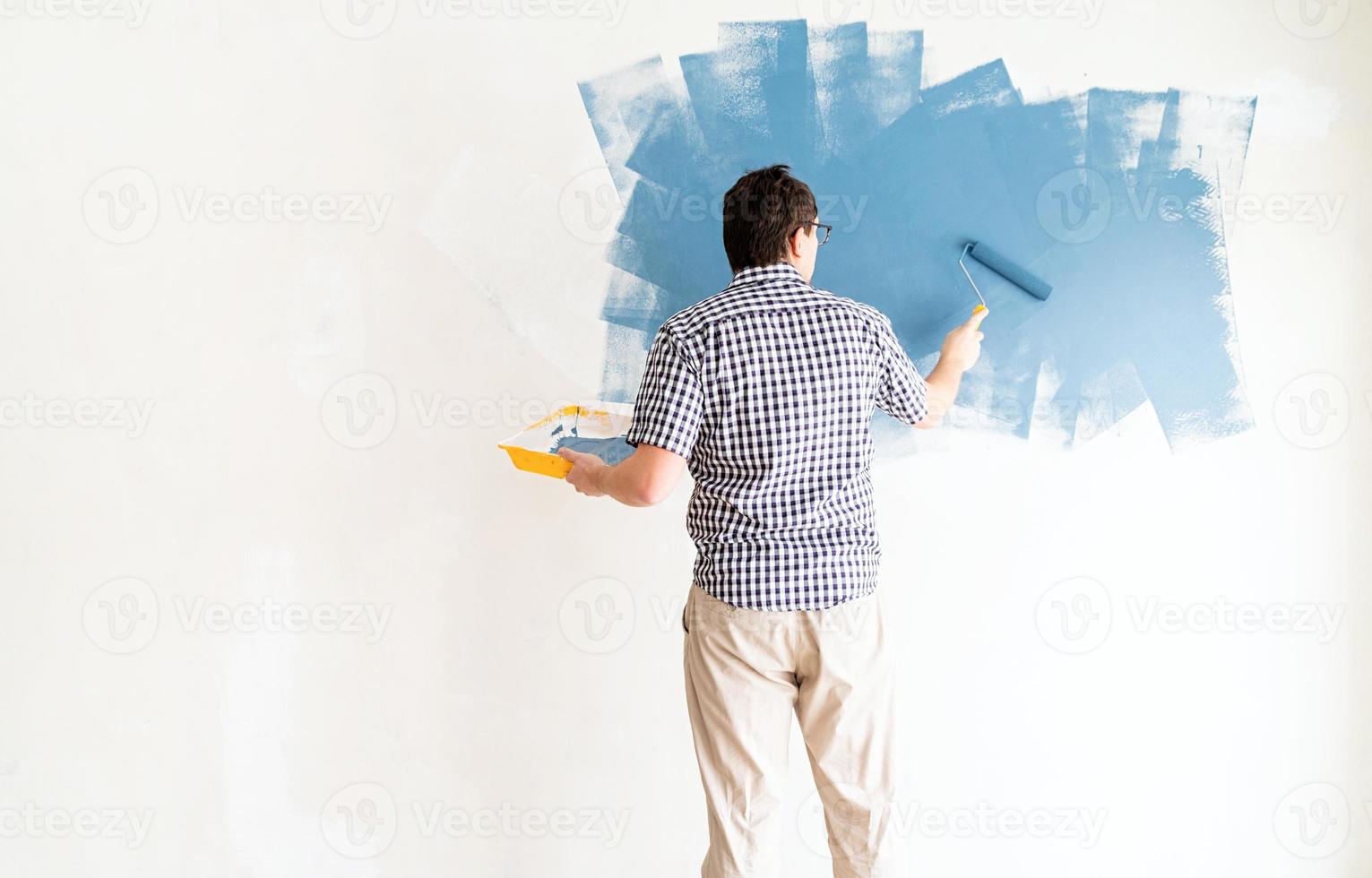 Hombre coloreando la pared azul con un rodillo foto