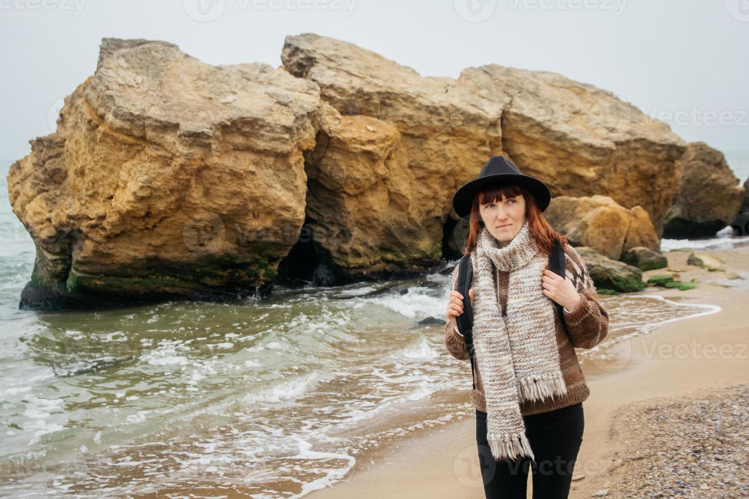 Woman in a hat with a backpack on background of sea and rocks photo