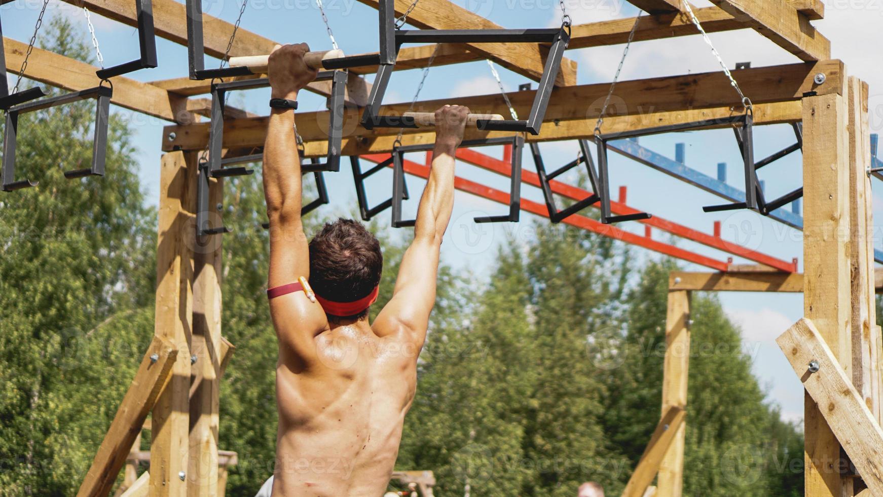 El hombre atravesando obstáculos durante la carrera de obstáculos en el campo de entrenamiento foto