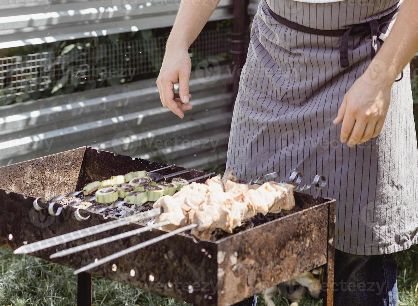 Joven asando brochetas en brochetas, hombre asando carne al aire libre foto