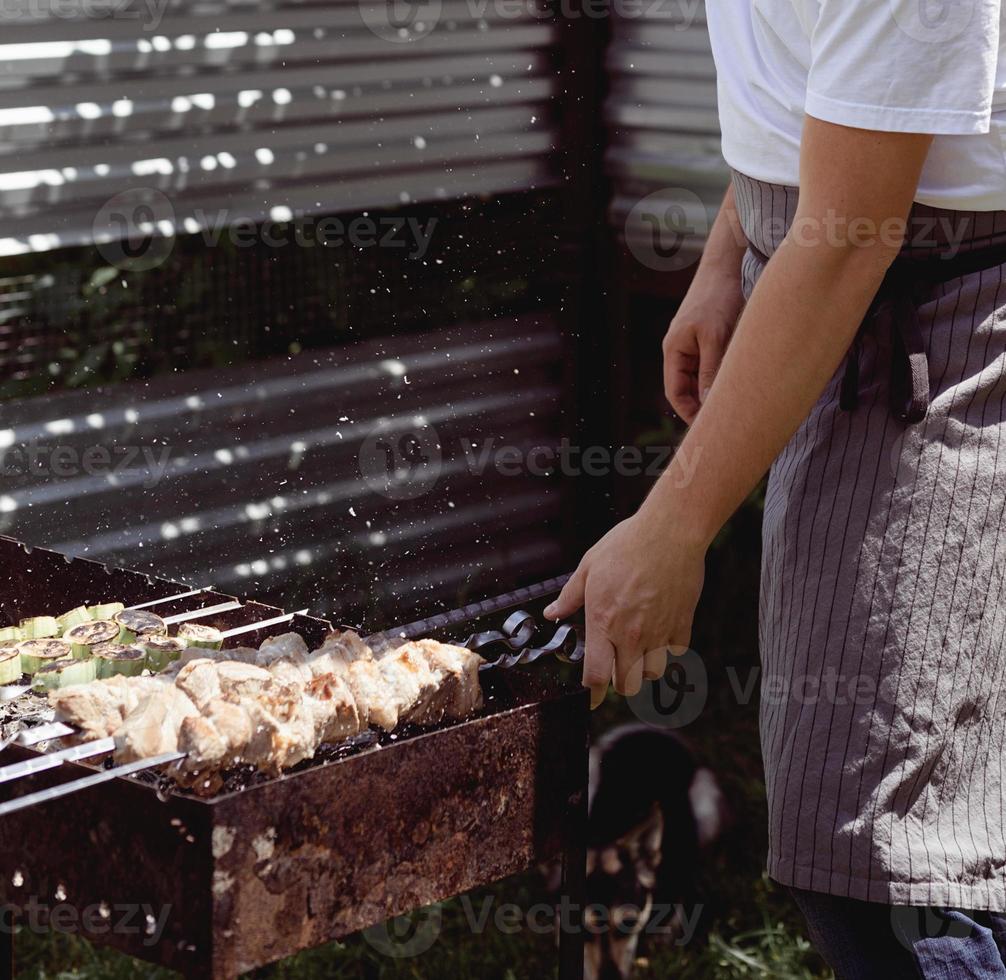 Close up of kebabs on skewers, man grilling meat outdoors photo