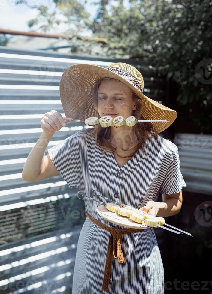 Mujer joven con sombrero de verano oliendo verduras asadas al aire libre foto