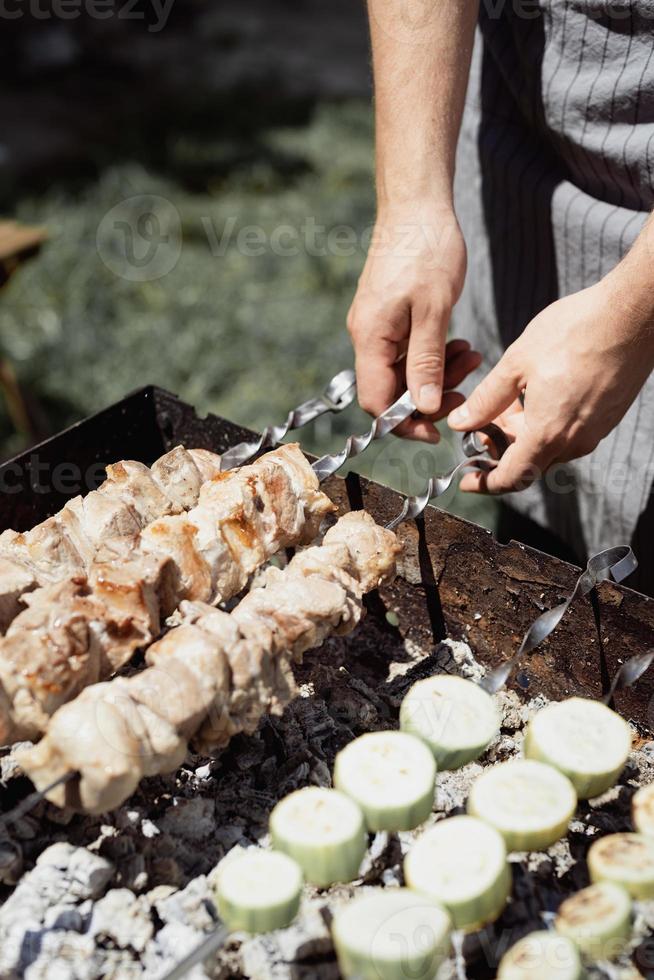 Cerca de kebabs en brochetas, hombre asando carne al aire libre foto