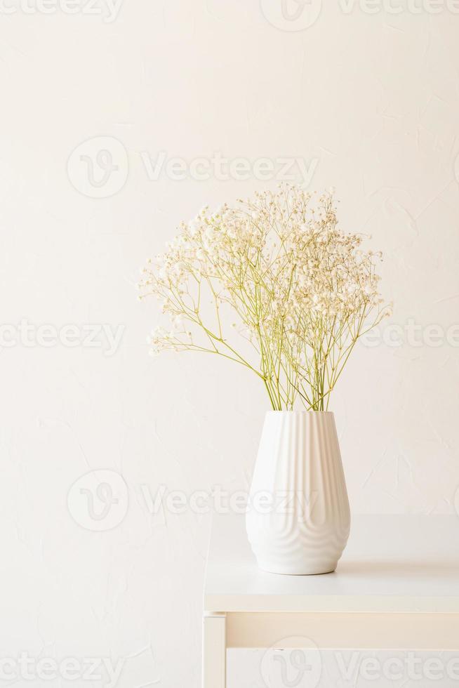 Flores blancas de gypsophila en jarrón blanco sobre la mesa, estilo minimalista foto