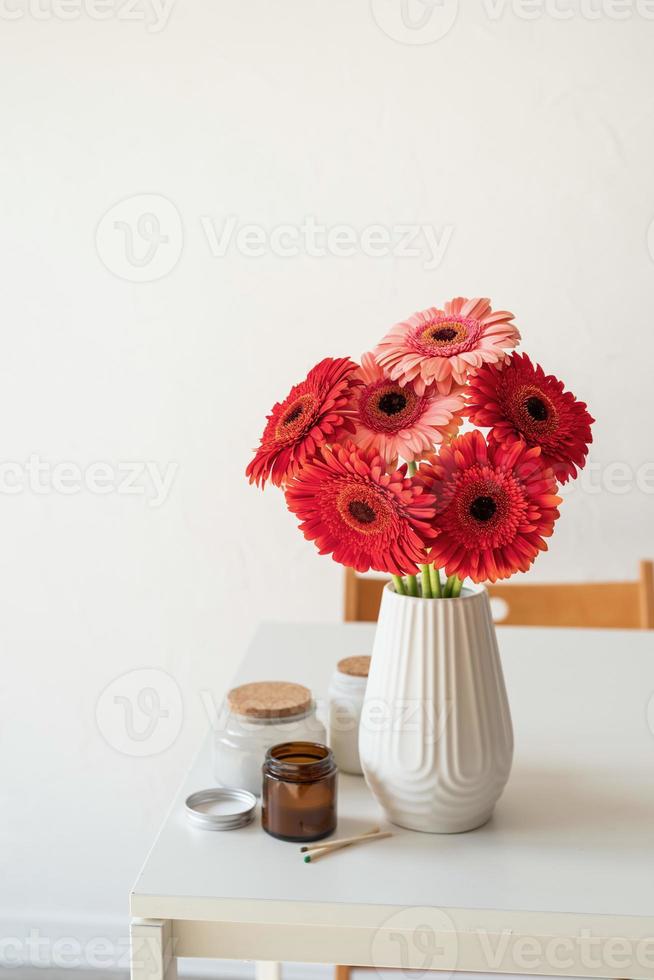 Margaritas gerberas brillantes en jarrón blanco sobre mesa, estilo minimalista foto