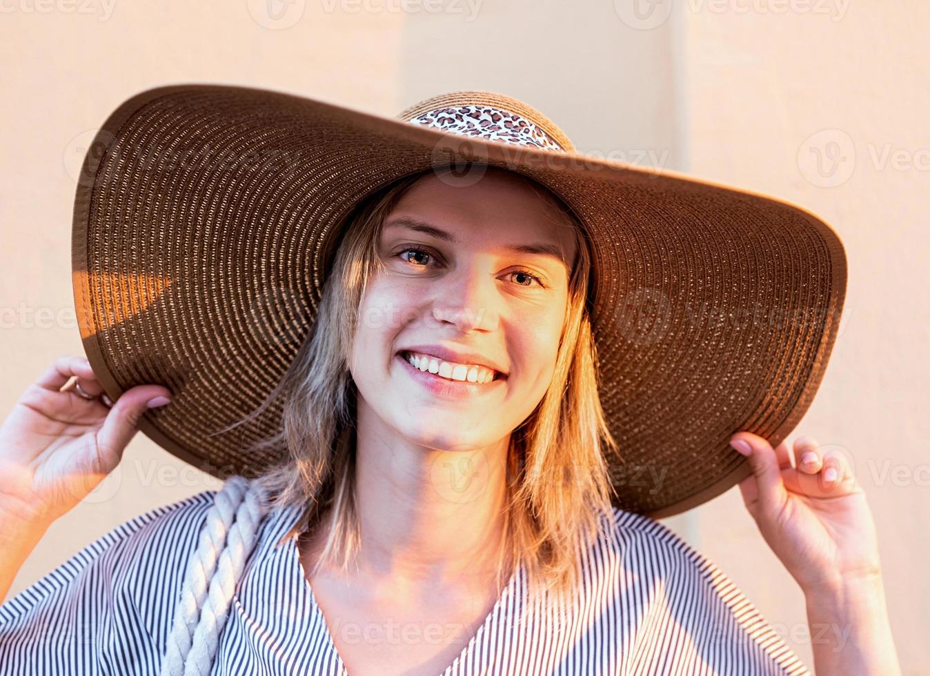 Cheerful woman in summer clothes holding her hat looking at the camera photo