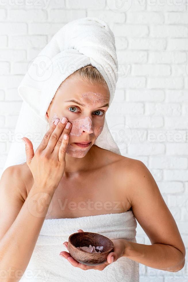 Young caucasian woman wearing white towels applying scrub on her face photo