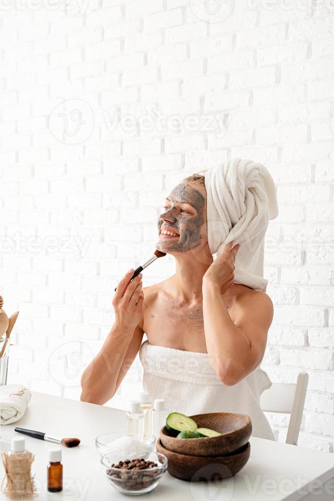 Young woman applying spa facial mask on her face with a cosmetic brush photo