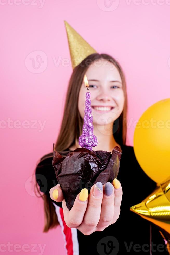 Chica adolescente sosteniendo muffin con una vela, pidiendo un deseo foto