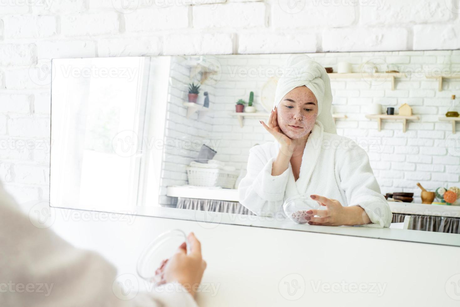 Feliz joven aplicando exfoliante facial en la cara foto